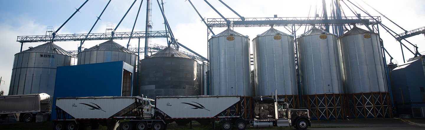 Side view of the Tem Ag Center with a grain hauling truck pulled up alongside some silos.